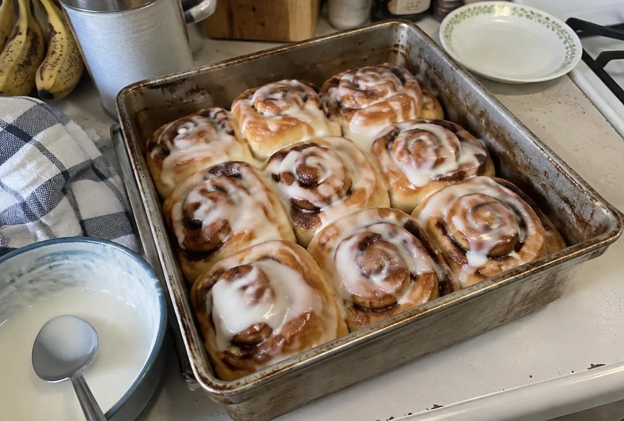 Pan of freshly baked cinnamon rolls with icing on a kitchen counter