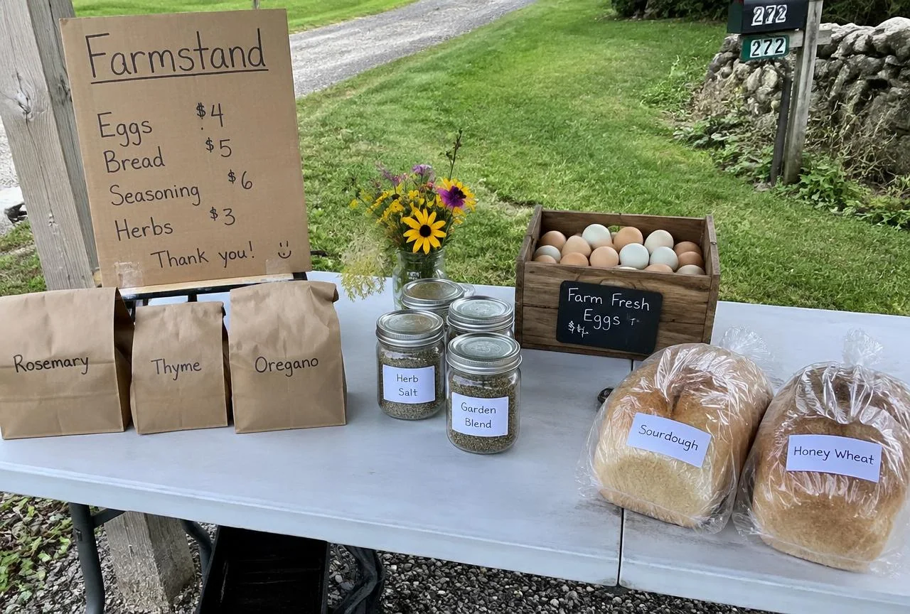 Small roadside farmstand table with bread, eggs, and seasoning jars